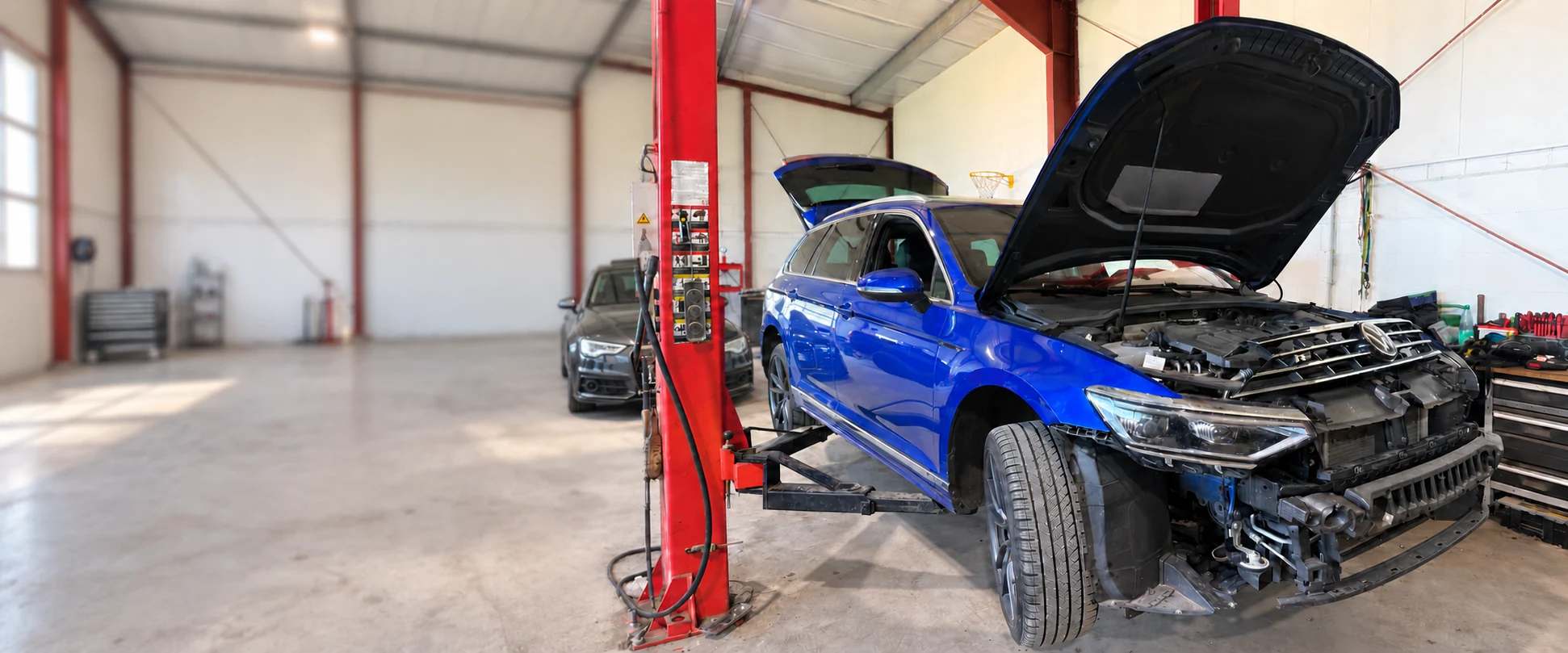 Blauer Volkswagen mit geöffneter Motorhaube und demontierter Front bei der Begutachtung in der Werkstatt
